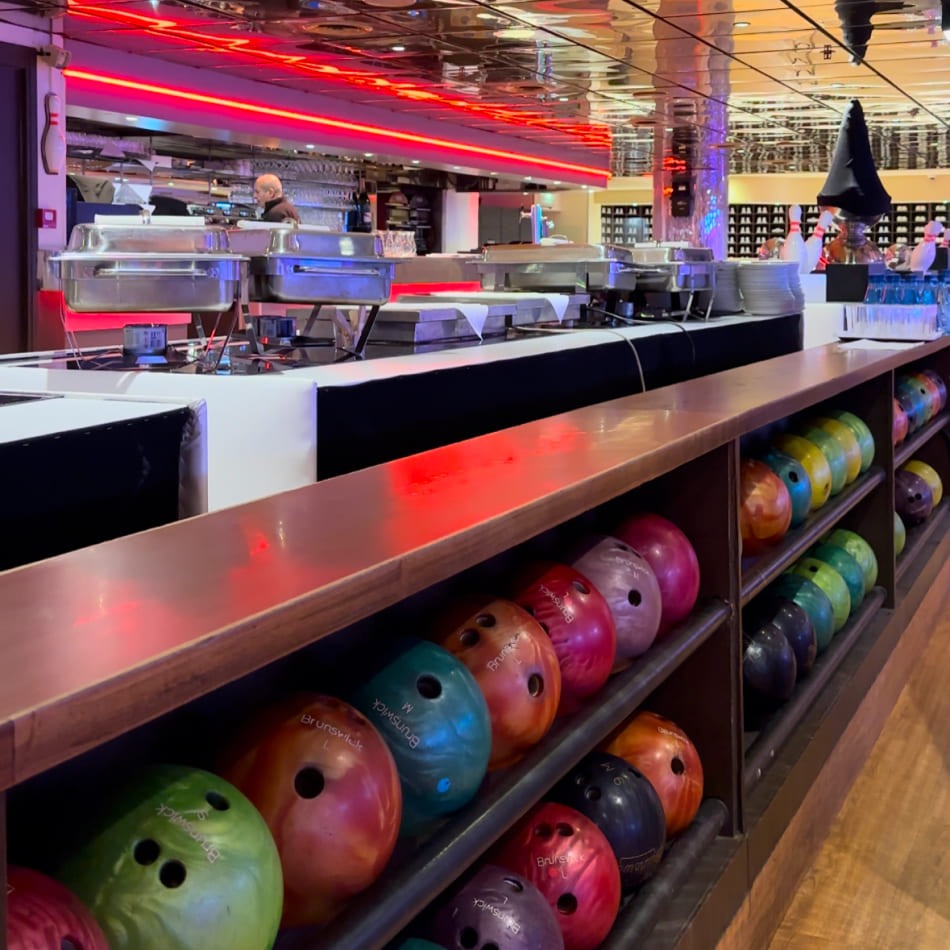 Buffet de restauration installé le long d'une piste de bowling, montrant des plats chauds et des boules de bowling colorées.
