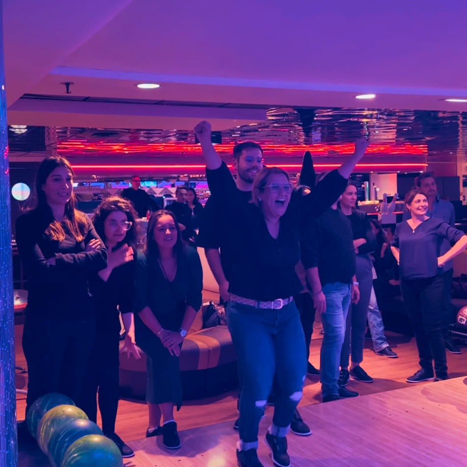 Une femme exprime sa joie les bras levés lors d'une partie de bowling en groupe dans une ambiance tamisée.