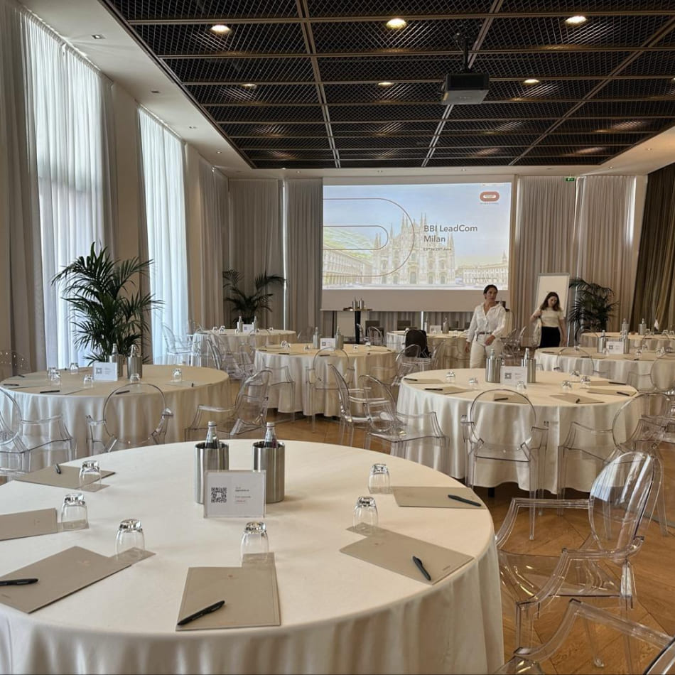 Salle de séminaire spacieuse avec tables rondes dressées et écran de projection affichant une présentation sur Milan.