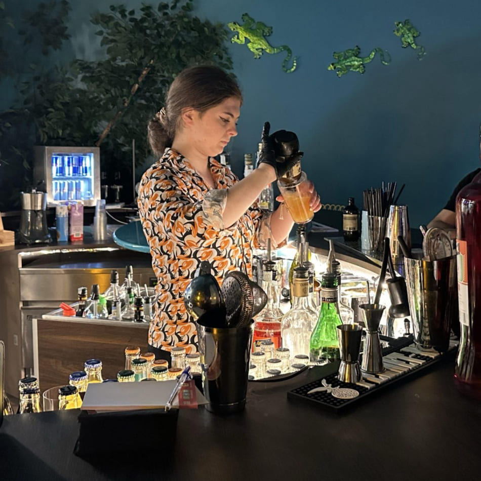 Barmaid en train de préparer méticuleusement un cocktail au shaker derrière un bar bien achalandé.