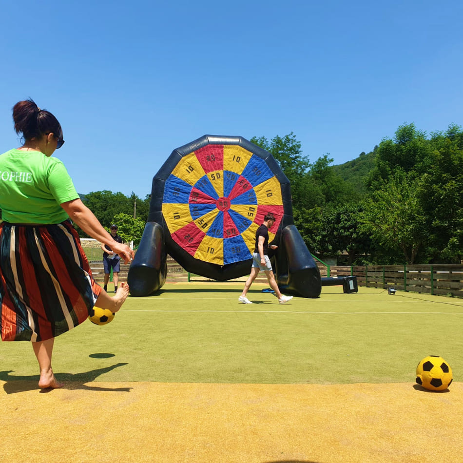 Femme s'apprêtant à tirer dans un ballon de football face à une cible géante gonflable en extérieur.