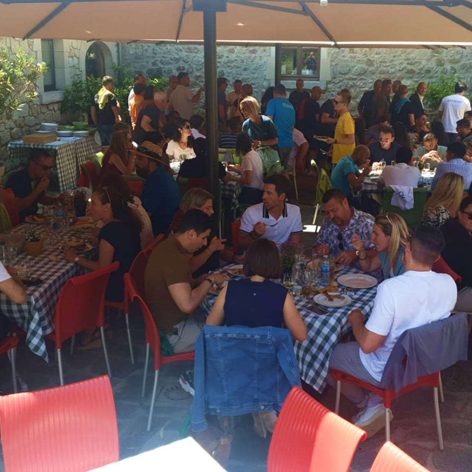 De nombreuses personnes attablées en terrasse sous des parasols lors d'un déjeuner convivial en extérieur.