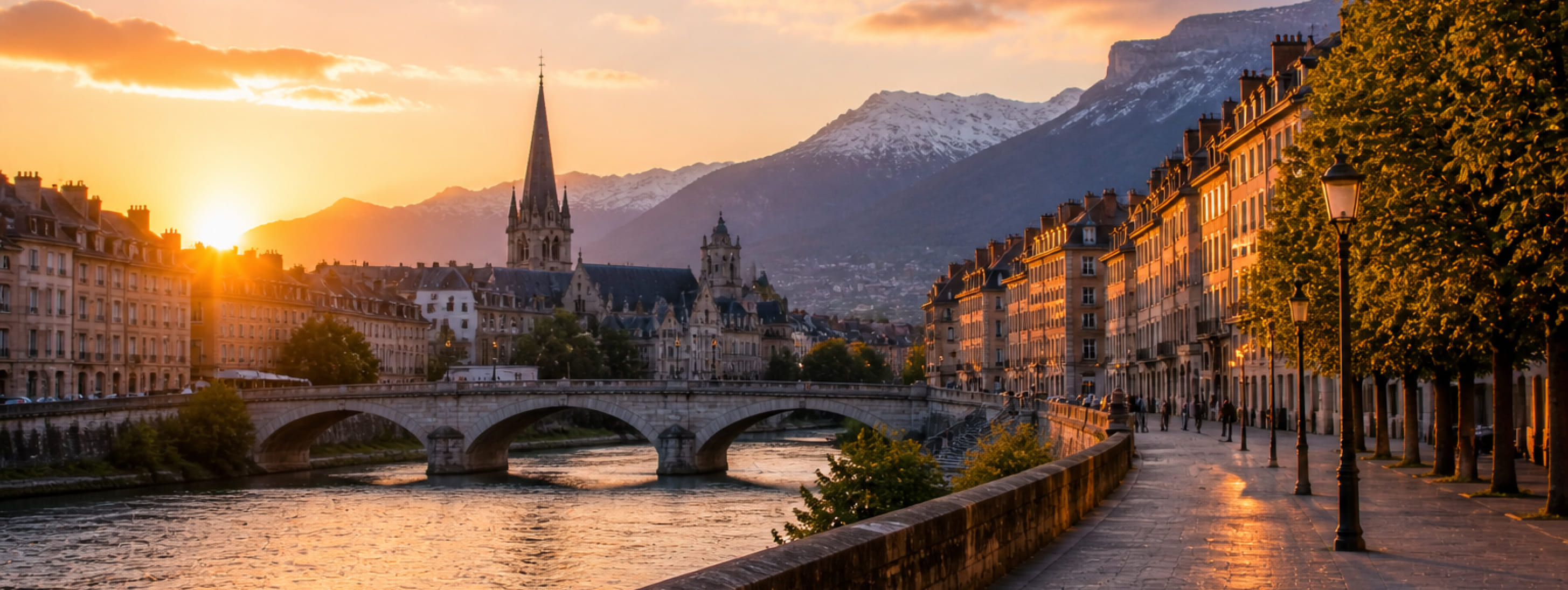 Coucher de soleil sur Grenoble montrant les quais de l'Isère, le pont Marius-Gontard et la flèche de l'église Saint-André avec les montagnes du Vercors enneigées en arrière-plan.