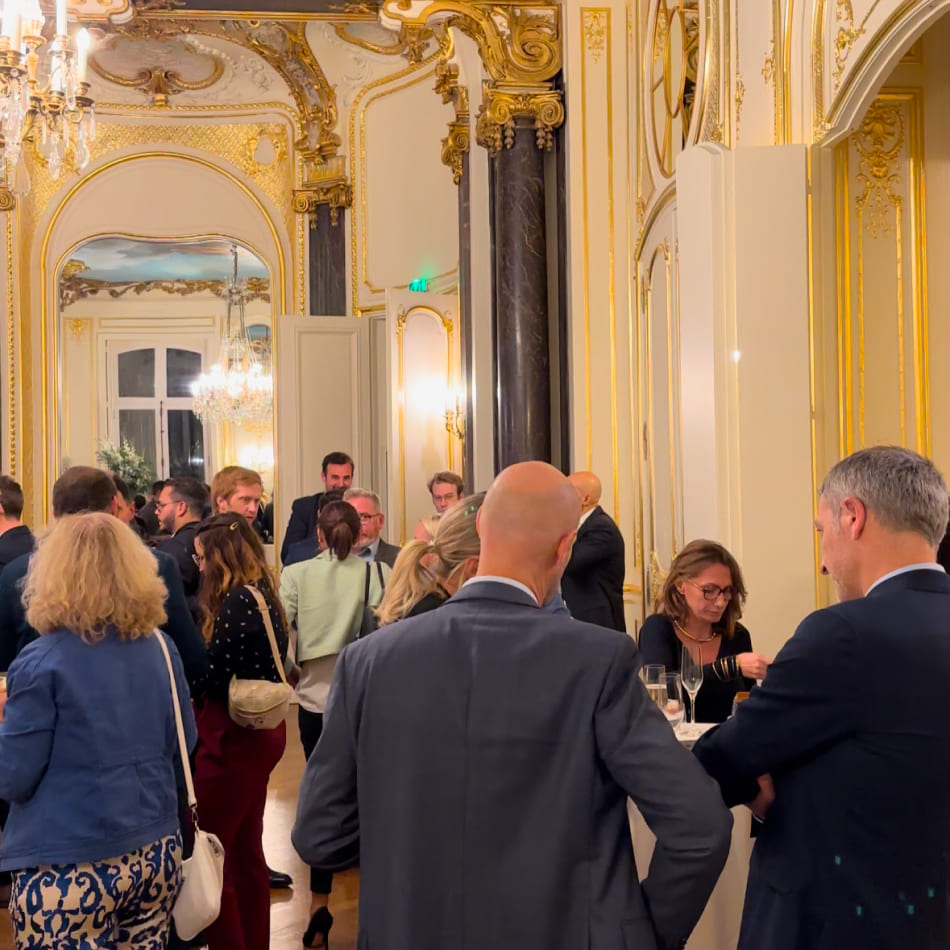 Réception élégante dans un salon de style classique avec de nombreux invités discutant debout.