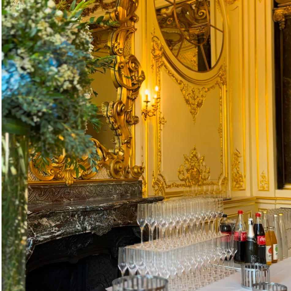Buffet de boissons avec des flûtes à champagne prêtes à être servies dans un décor luxueux aux dorures raffinées.