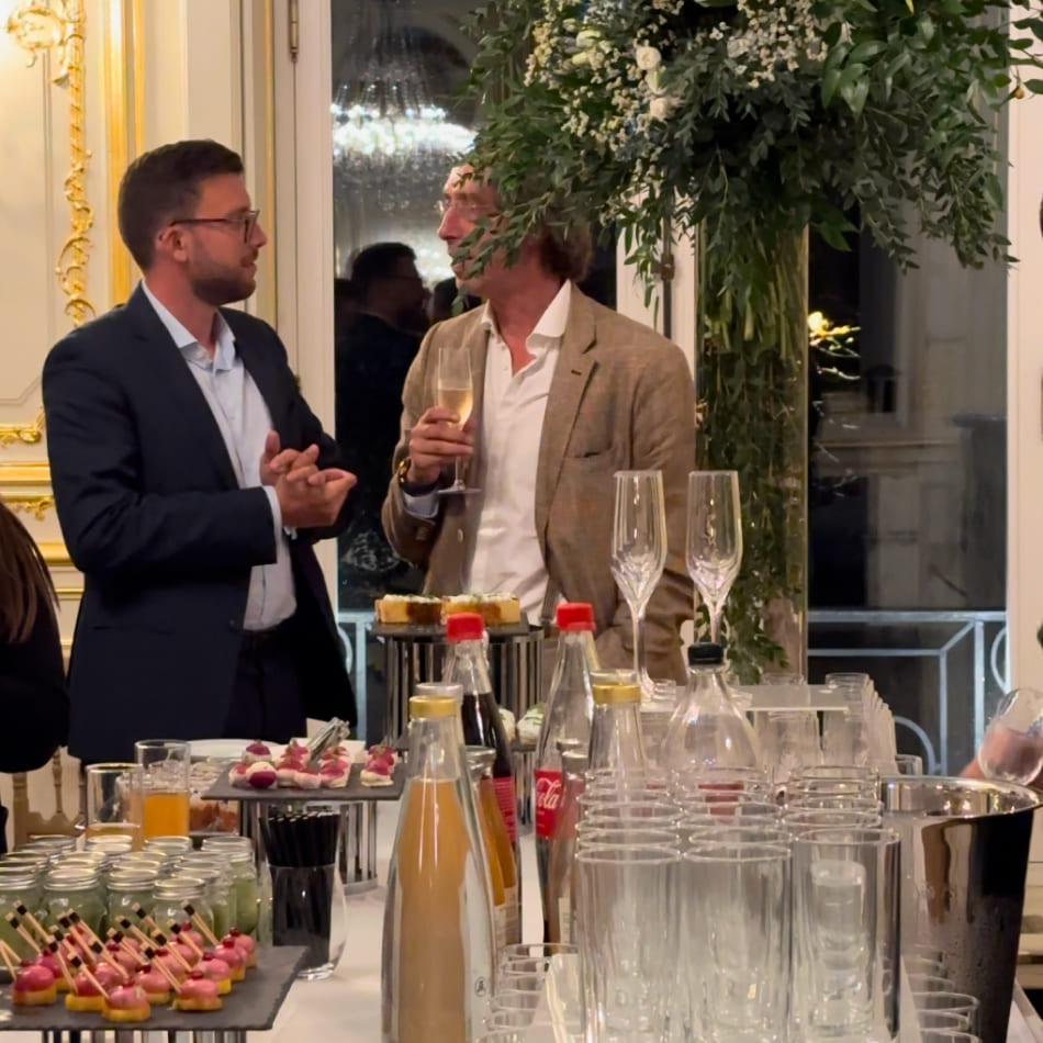 Deux invités en tenue de soirée discutent près d'un buffet de cocktail dînatoire élégamment présenté.