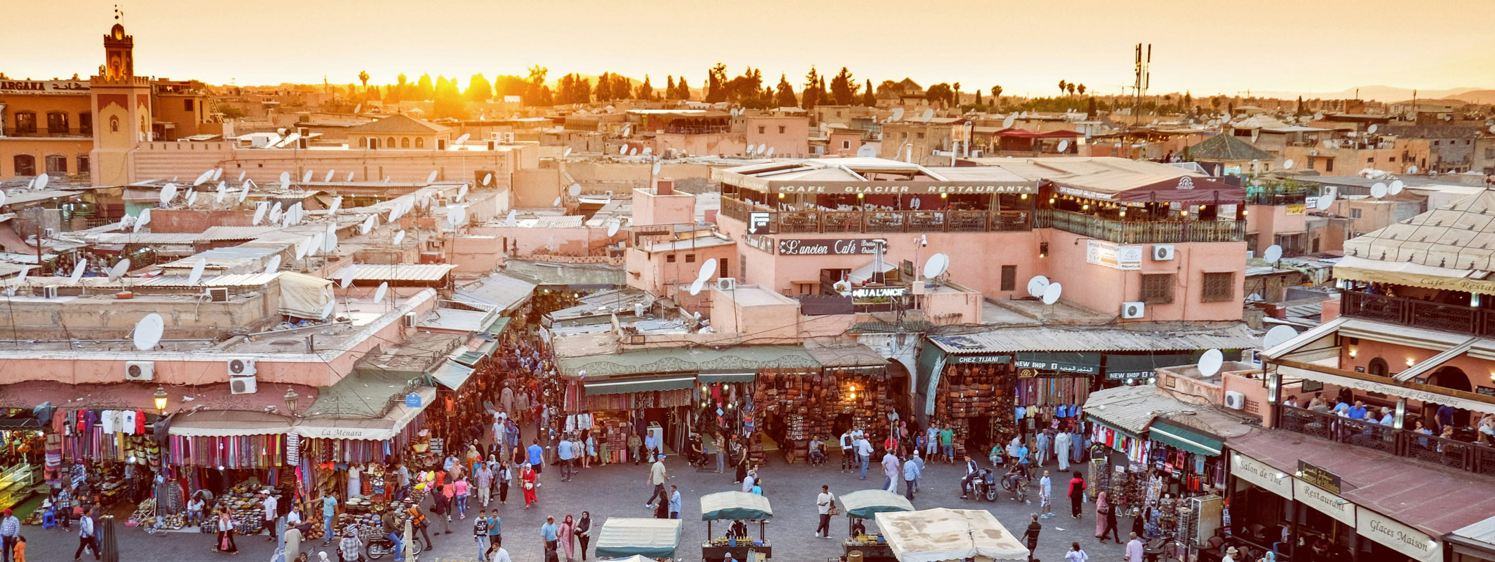 Place Jemaa el-Fna à Marrakech animée par la foule et des étals de marché sous une lumière dorée.