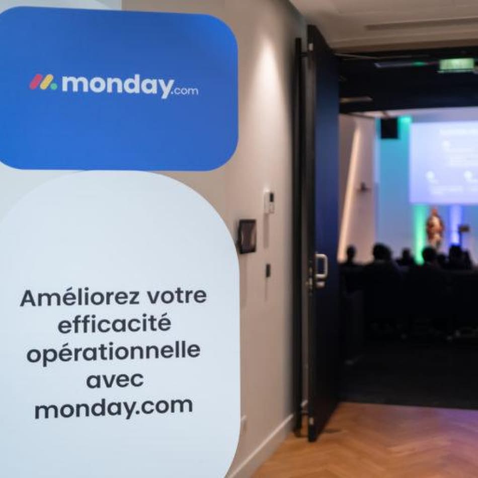 Affiche promotionnelle pour la solution monday.com devant l'entrée d'une salle de conférence.