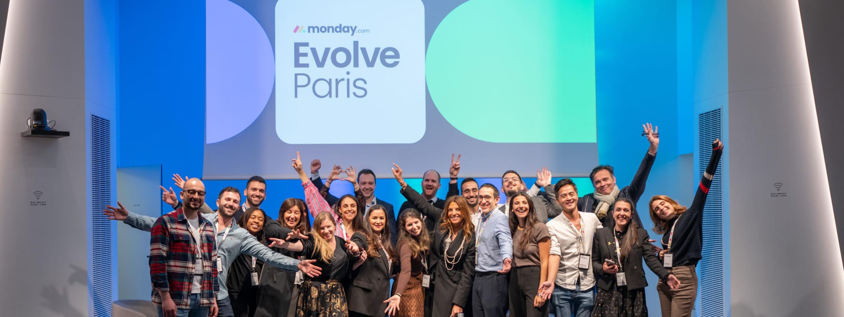 Photo de groupe joyeuse de l'équipe organisatrice sur scène devant l'écran géant de l'événement "Evolve Paris".