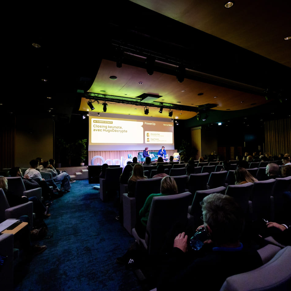 Vue d'une salle de conférence sombre où le public écoute une présentation intitulée "Closing keynote avec HugoDécrypte".
