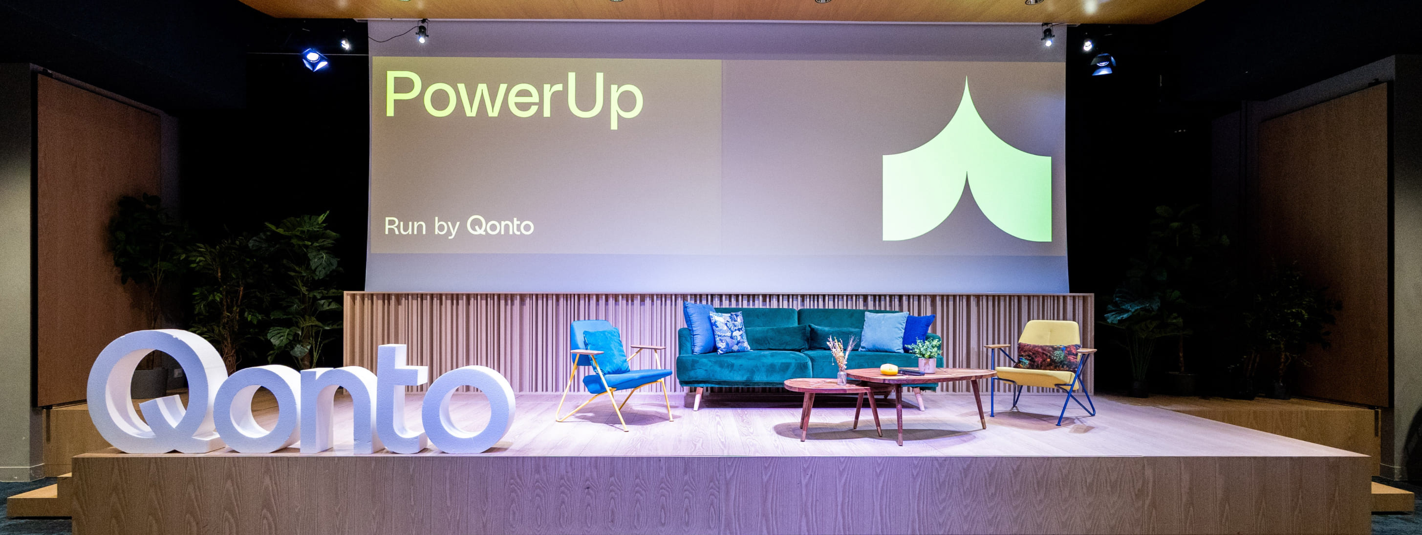 Scène vide décorée de fauteuils colorés et du logo "Qonto" en grandes lettres blanches devant un écran géant "PowerUp".