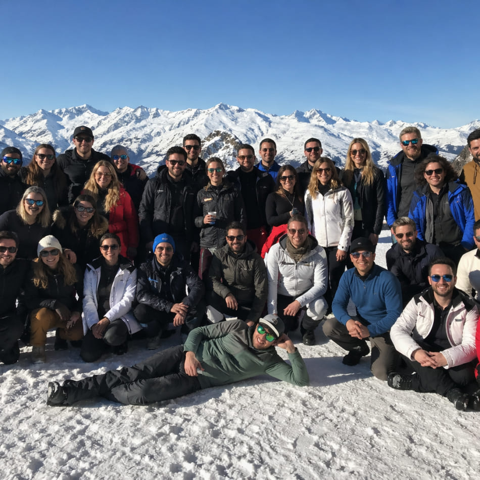 Quatre participants en tenue de randonnée hivernale, vus de dos, admirant une chaîne de montagnes enneigées. L'un d'eux pointe du doigt un sommet lointain.