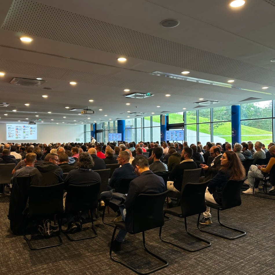 Large audience de professionnels assis dans une salle de conférence lumineuse face à une présentation sur écran.