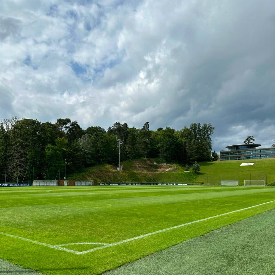 Vue d'ensemble d'un terrain de football professionnel parfaitement entretenu sous un ciel nuageux.