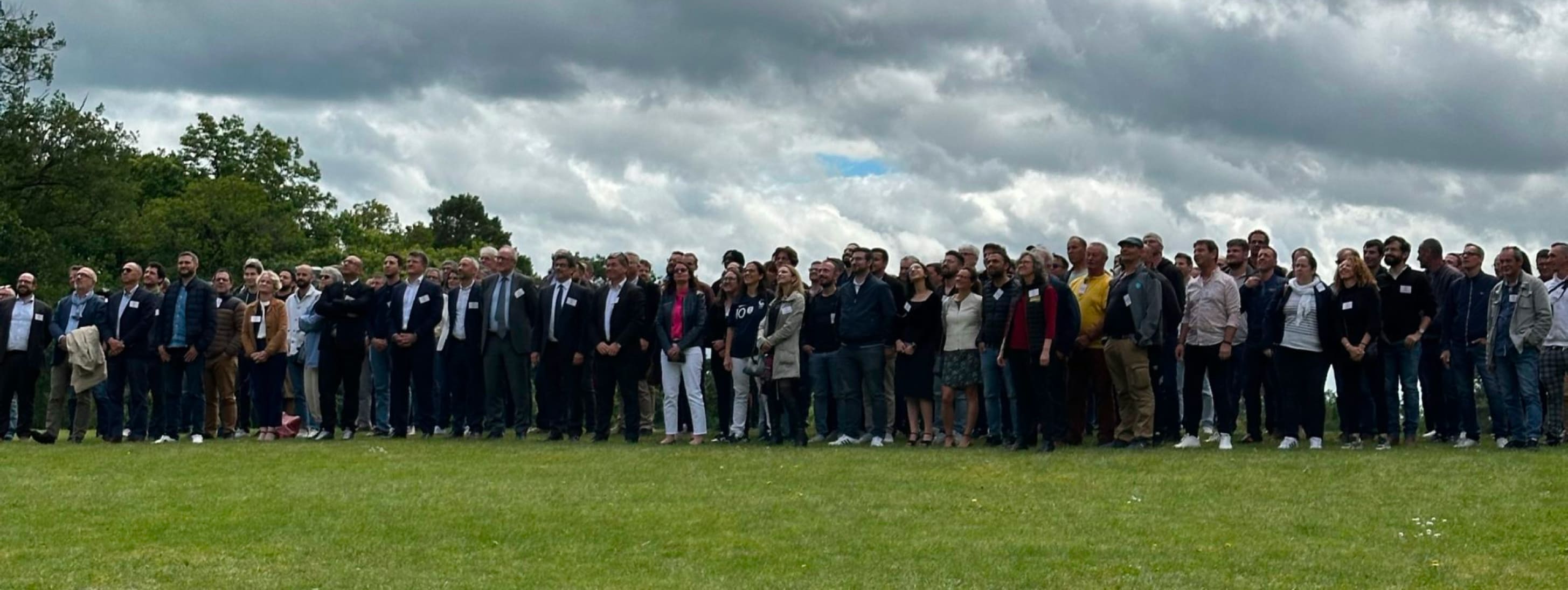 Grande assemblée de participants debout en extérieur sur une pelouse pour une photo de groupe institutionnelle.